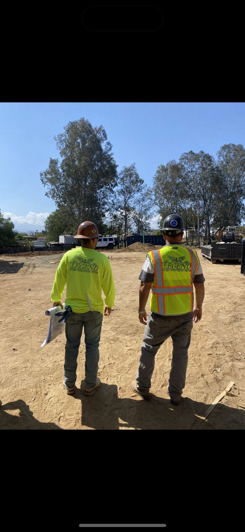 Two Legend Pipeline crew members in branded hi-vis walking a jobsite with plans in hand